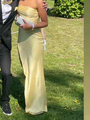 Ljusgul balkänning - Supersnygg ljusgul uppsydd balklänning med öppen rygg, off the shoulder och slits. material med axelbandslös design och hög slits framtill. Klänningen har öppen rygg och en elegant, figurnära passform som ger en riktigt lyxig känsla. 