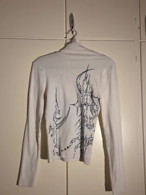 Finns en i hela världen polotopp  - Finns en i hela världen. Säljer en vit långärmad polotopp från BikBok i storlek S. Toppen har ett unikt svart grafiskt mönster  och är gjord i mjuk ribbad bomull med lite stretch för skön passform. Perfekt för dig som gillar coola detaljer och vill sticka ut. 