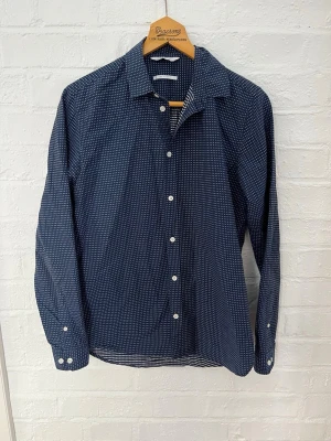 Mörkblå prickig skjorta Samsøe Samsøe - Snygg mörkblå skjorta från Samsøe Samsøe med vita prickar och klassisk krage. Slim fit-modell med långa ärmar och vita knappar framtill. Perfekt för dig som gillar stilrena detaljer och en smalare passform.