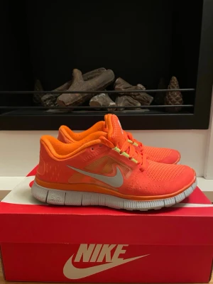 Nike Free Run 3 orange sneakers - Nike Free Run 3 sneakers i en riktigt poppig orange färg med vita detaljer och mesh-ovandel för extra andningsförmåga. Skorna har vita sulor och limegröna detaljer vid snörningen. 
