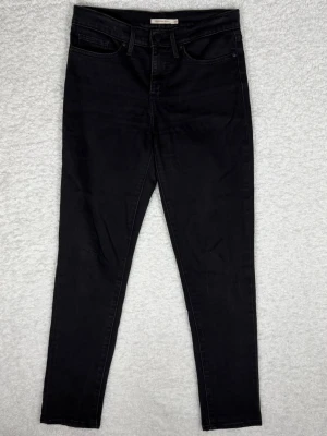 Levi's 311 shaping skinny jeans svart - Svarta Levi's 311 shaping skinny jeans med klassisk femficksdesign och smal passform. Hög midja och stretchigt jeansmaterial som sitter snyggt och bekvämt. Perfekt för dig som gillar en stilren look med tajt siluett.