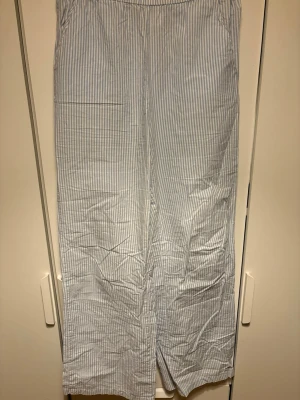 Randiga linnebyxor från Kappahl XS - Säljer ett par ljusblå och vita linnebyxor från Kappahl i storlek XS. Byxorna har ett avslappnat loose fit, elastisk midja och ett klassiskt randigt mönster. Perfekta för varma dagar och chill stunder. Materialet är mjukt linne som andas.