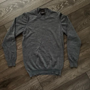 Grå stickad tröja från Oscar Jacobson - Snygg grå stickad tröja från Oscar Jacobson i storlek S. Tröjan har rund halsringning, ribbade muddar vid ärmslut och nederkant samt långärmad passform. Perfekt för dig som gillar stilrena och klassiska plagg med en modern touch.