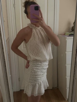 Vit kortklänning med volang från SHEIN - Supersöt vit kortklänning från SHEIN med volangdetaljer och smockad halsringning. Klänningen har ett subtilt mönster, pärlknappar i nacken och är ärmlös. Skulle säga att den är något liten i storlek då jag vanligtvis bär storlek S🤍