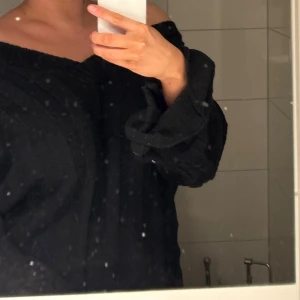 Svart offshoulder stickad tröja - Säljer en svart stickad tröja med offshoulder-design och bred v-ringning. Tröjan har långa ärmar och en loose passform som ger en avslappnad och trendig look. Perfekt för dig som gillar oversized och mysiga plagg.