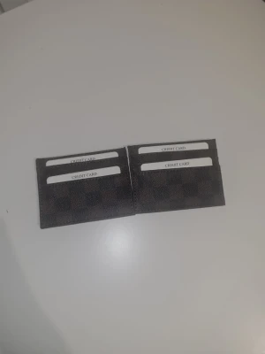 Brun rutig plånbok i skinn - Snygg och smidig plånbok i brunt skinn med rutigt mönster. Perfekt för kort och enkel att ha med sig i fickan. Plånboken har flera fack för kreditkort och är stilren med en klassisk design. Fastpris 