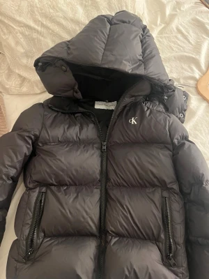 Svart pufferjacka från Calvin Klein Jeans - Säljer en svart vinterjacka från Calvin Klein. Jag köpte den förra året och nu har jag vöxt ur den. Den är knappast använd så den är i fint skick. Det är storlek xs men den är ganska liten i storleken. Hör av er om ni har frågor. Den kostade ca 1 600 kr när vi köpte den.