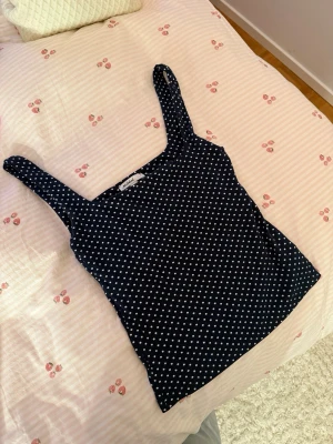 Mörkblå prickig linnetopp Subdued - Säljer en mörkblå linnetopp från Subdued i storlek S. Toppen har vita prickar över hela och breda axelband. Materialet är mjukt och stretchigt, perfekt för sommaren. Snygg att styla med jeans eller kjol för en chill look.