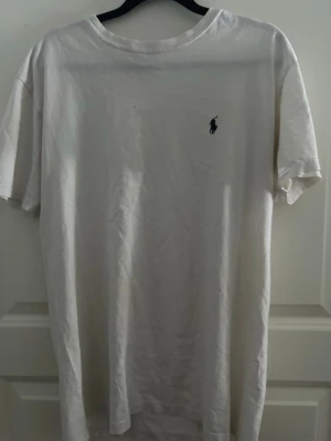 Vit och marinblå t-shirt från Polo Ralph Lauren - Två klassiska t-shirts från Polo Ralph Lauren. En vit med liten mörkblå logga på bröstet och en marinblå med röd logga. Båda har rund hals och korta ärmar, tillverkade i mjuk bomull. Perfekt för en clean och stilren look. Vita i storlek S och blåa barnstorlek XL passar den som är runt 170. Vita T-shirten har två små hål en på framsidan och en på baksidan därför får man båda för 200 och vita för 50kr och blåa för 175kr
