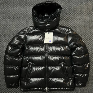 Svart Moncler Maya  - Säljer en snart Moncler Maya i toppskick. Otroligt varm, lätt och stilren – perfekt för både vardag och stad. Jackan har den ikoniska glansiga ytan, Moncler-loggan på ärmen 