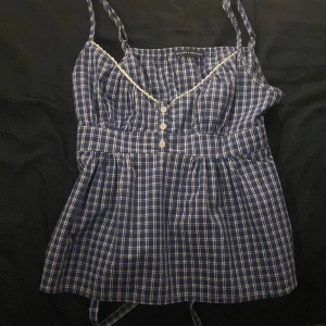 Blå rutig linnetopp Brandy Melville - Andvänt 1-2 gånger, ordinarie pris 280kr. Supersöt blå linnetopp från Brandy Melville med vitt rutmönster och tunna axelband. Toppen har dekorativa vita knappar framtill, spetsdetalj vid halsringningen och markerad midja. Perfekt för varma dagar och chill vibes.