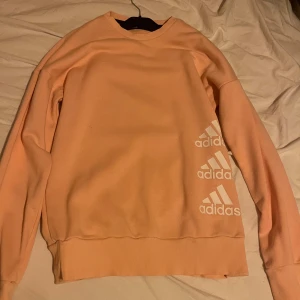 Persikofärgad sweatshirt från Adidas - Säljer en persikofärgad sweatshirt från Adidas med tre vita Adidas-loggor på sidan. Den är inte använd så gott som ny 🙌🏼