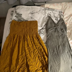 Gul och grön klänning med twistdetalj - Två klänningar säljes! En gul axelbandslös klänning med smock upptill och vid kjol, perfekt för sommar. Den andra är en lång grå klänning med smala axelband och snygg twistdetalj framtill, samt ribbad struktur. 