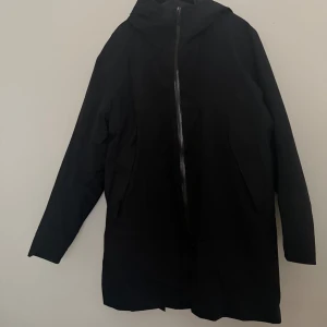 Svart parkajacka från Arc'teryx Veilance XL - Svart parkajacka från Arc'teryx Veilance i storlek XL. Jackan har huva, hel dragkedja framtill och två sidofickor. Materialet är syntet och designen är stilren och minimalistisk, perfekt för dig som gillar funktion och enkelhet.