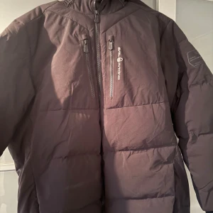 Svart pufferjacka Sail Racing XXL (Passar XL) - Svart pufferjacka från Sail Racing, modell Antarctica Expedition. Jackan har huva, två bröstfickor med dragkedja och Sail Racing-logga på bröstet samt patch på ärmen. Perfekt för kalla dagar med sin tjocka vaddering och stilrena look.  Nypris 5000kr