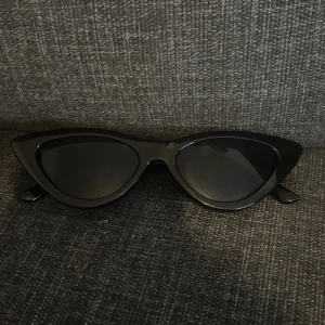 Solglasögon  - Snygga svarta solglasögon i klassisk cat eye-modell. De har en glansig finish och smala bågar som ger en cool och trendig look. 