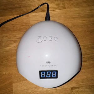 BeautyLushh UV LED Nagellampa - Effektiv UV LED nagellampa från BeautyLushh med digital display och timerfunktion (10s, 30s, 60s). Lampan är i gott skick med mindre ytliga repor. Perfekt för gelnaglar och professionell manikyr hemma. Fungerar utmärkt, testad och klar att användas.