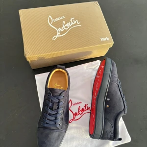 Christian Louboutin  skor  - Snygga mörkblåa  sneakers från Christian Louboutin i mocka med klassisk röd sula och diskret logga på sidan. Skorna har rund tå, snörning och platt sula. Perfekta för dig som vill ha en lyxig och stilren look med en touch av Paris.