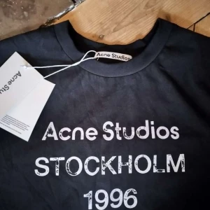 Svart långärmad Acne Studios tröja - Svart långärmad tröja från Acne Studios med vit tryckt text 'Acne Studios Stockholm 1996' på bröstet. Rund hals och mjukt bomullsmaterial. Perfekt för dig som gillar stilrena och ikoniska plagg med streetkänsla. Pris kan diskuteras!!!