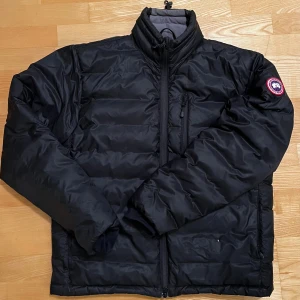 Canada Goose svart jacka L - Säljer en svart dunjacka från Canada Goose i storlek L. Jackan har hög krage, dragkedja framtill och en bröstficka med dragkedja. Klassisk Canada Goose-logga på ärmen. Perfekt för kalla dagar och riktigt snygg streetstil. Has Little hole otherwise 9/10 condition