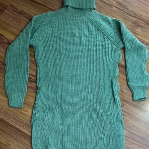 Grön stickad lång tröja  - Mysig grön stickad tröja med polokrage och långa ärmar. Tröja har ribbstickad struktur och är figurnära med slits i sidan. Perfekt för dig som gillar en enkel men snygg look under kallare dagar.