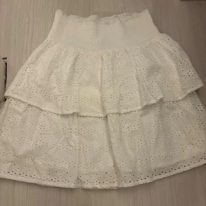 Vit volangkjol  - Supersöt vit kortkjol från spnhlt (gekås ullared) med broderade hål och volanger. Kjolen har bred smock i midjan för en bekväm passform och är gjord i bomull. Perfekt för dig som gillar romantisk och luftig stil. Pris kan diskuteras!