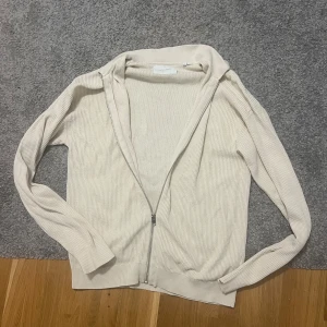 Beige ribbad kofta från Jack & Jones - Snygg beige kofta från Jack & Jones i storlek S. Tröjan är ribbad och har en dragkedja framtill, vilket gör den enkel att ta på och av. Långärmad och tillverkad i mjukt material som passar perfekt för chill dagar. Stilren och enkel design.