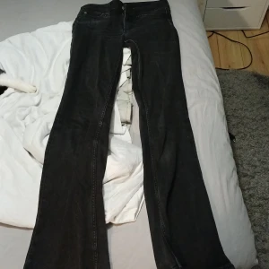 Svarta bootcut Cheap Monday jeans 27/32 - Säljer ett par svarta jeans från Cheap Monday i modellen bootcut. De har svarta sömmar och en cool lila logga på bakfickan. Materialet är en mix av bomull och polyester som ger stretch och skön passform. De är lite utvättade och då alltså lite gråa i tonen.