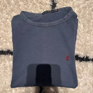 Blå tröja från Polo Ralph Lauren - Snygg mörkblå tröja från Polo Ralph Lauren med klassisk röd logobrodyr på bröstet. Rund hals och mjukt bomullsmaterial gör den skön att bära. Perfekt för dig som gillar stilrena och tidlösa plagg. Vid snabb affär sänks priset!! Det är i mellan bra skick och mycket bra!!