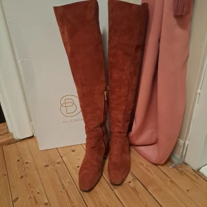 Bruna mocka overknee stövlar Baldowski - Snygga overknee stövlar från Baldowski i brun mocka med bred klack och rund tå. Stövlarna har dragkedja på insidan och en mjuk, lyxig känsla. Perfekt för dig som vill sticka ut med höga boots i höst och vinter.Superfina äkta mocka stövlar med skinn inner detaljer i storlek 38. Är true i size som passar vanliga 38or. Helt felfria och super snygga på 🤩 behaglig klack höld 6cm och går upp till knähöjd. 