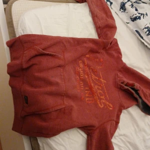 Röd hoodie med tryck från Petrol Ind - Röd hoodie från Petrol Industries med  tryck på bröstet och coola detaljer vid huvan. Tröjan har känguruficka framtill och långa ärmar. Perfekt för dig som gillar  att ha något bekvämt och snyggt.