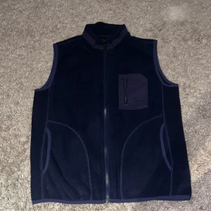 Mörkblå fleeceväst med dragkedja. Inget varumärke. - Mörkblå fleeceväst med hög krage och hel dragkedja framtill. Västen har två sidofickor och en bröstficka med dragkedja i matchande tyg. Perfekt för lager-på-lager och chill dagar.