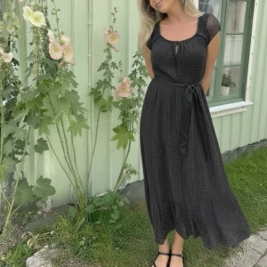 Svart prickig långklänning Esprit - Supersöt svart långklänning från Esprit med vita prickar, transparenta korta ärmar och knytning vid urringningen. Klänningen har ett avtagbart midjeband.