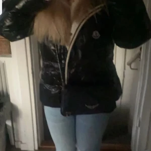 Svart pufferjacka från Moncler - Säljer en svart pufferjacka från Moncler med glansig finish och vita detaljer vid dragkedjan. Jackan har quiltad design, lång ärm och klassisk Moncler-logga på bröstet. Perfekt för dig som gillar streetstyle och vill ha en varm jacka med snygg look. Jag kan sälja den för ett bra pris och om någon vill byta så kan jag gärna göra det, det verkar så att jackan är för står för mig och har aldrig använt den !❤️