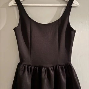 Svart linne från NA-KD - Svart linne från NA-KD med rundad halsringning och markerad midja. Den lätt rynkade midjan ger en snygg volym. Perfekt för dig som gillar en egdy men samtidigt gullig look.