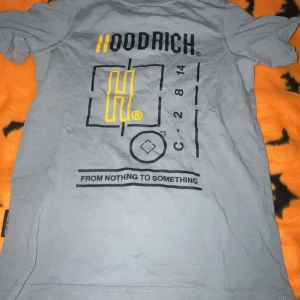 Grå Hoodrich t-shirt med tryck - Snygg grå t-shirt från Hoodrich med stort grafiskt tryck och texten 'FROM NOTHING TO SOMETHING' på ryggen. Framsidan har Hoodrich-logga i svart och gult. Klassisk passform och rund hals. Perfekt för dig som gillar streetwear.