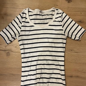 Randig vit topp från Amisu - Säljer en fräsch vit topp från Amisu i storlek S med svarta horisontella ränder. Toppen har rund halsringning och korta ärmar. Materialet är ribbad bomull som känns mjukt mot huden och ger en snygg passform.