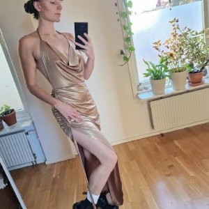 Guldig klänning med slits - Ursnygg långklänning i guldigt tyg med draperad urringning, öppen rygg och knyt i nacken. Hög slits på sidan som kan justeras för mer/mindre rouge. Ett fantastiskt tillskott för vilken kväll som helst 🧡💃 står M, men även S skulle kunna ha den. Återuppladdad för fri frakt. Jag har mycket annat uppe på sidan, både herr och damkläder. Köp gärna bundle för att få rabatt 🤗