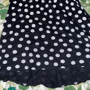 Svart prickig klänning XS - Supersöt svart kjol från Blanche Story i storlek XS med stora vita prickar. Modellen är kort och har en lätt volang nertill. Perfekt för dig som gillar lekfulla mönster och vill sticka ut lite extra. Tunn och skön, passar bra till varmare dagar.