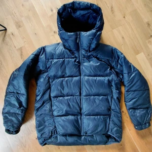 Mörkblå pufferjacka från J.Lindeberg - Säljer en mörkblå pufferjacka från J.Lindeberg med huva och dragkedja. Jackan är vadderad med PrimaLoft Gold Insulation för extra värme och har en clean, boxig look. Perfekt för kalla dagar och enkel att matcha med olika outfits. Den är i super bra skick och har inga defekter som jag känner till, kom gärna med frågor!😁