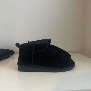 Svarta vinterskor ”uggs” - Säljer ett par svarta vinterskor i mocka med platt sula. Skorna har en enkel och stilren design med låg skaft och dragflik bak. Perfekta för kalla dagar och passar till många olika outfits. Säljer dessa då jag fått två par av de. nypris 500