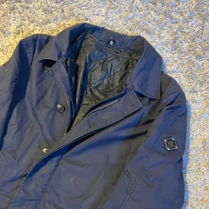 J.Lindeberg trenchcoat kappa marinblå herr S - J.Lindeberg trenchcoat i storlek S. Bra skick generellt förutom att en knapp saknas. Mörks inte när man bär, enkelt att sy ihop. Har ett innerfoder som går att ta ut vid varma dagar. Postas antigen samma dag som köp eller dagen därpå🙌💯