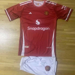 Manchester United Garnacho matchtröja - Manchester Uniteds officiella matchtröja med Garnacho 17-tryck. Röd med vita detaljer, klubbmärke och Adidas-logga på bröstet. Kortärmad och tillverkad i lätt, ventilerande funktionsmaterial. Säljes tillsammans med vita shorts med klubbmärke.