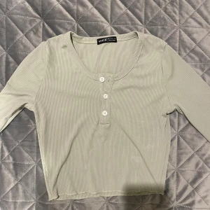 Ljusgrön ribbad topp från SHEIN - Säljer en ljusgrön ribbad topp från SHEIN i storlek S. Toppen har lång ärm, rund halsringning och tre vita knappar framtill. Croppad passform som ger en chill vibe. Perfekt att styla med jeans eller kjol för en enkel look.💚