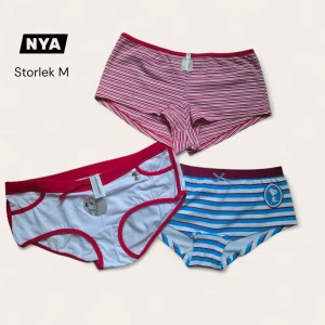 Nya Snoopy trosor M - Tre par mjuka trosor från Snoopy i storlek M. Ett par är röd- och vitrandiga med Snoopy-tryck och ficka, ett par är vita med röda detaljer och Snoopy-motiv, och ett par är blå- och vitrandiga med vinröd kant och Snoopy-tryck. Alla är tillverkade i bomull och har bekväm passform.