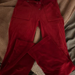 Röda Juicy Couture mjukisbyxor  - Röda mjukisbyxor från Juicy Couture i velour med breda ben, stora fickor fram och bak. Ikonisk logga broderad på ena fickan. Använda max tre gånger, inga fläckar eller märken. Köpta för ungefär 1000kr. 