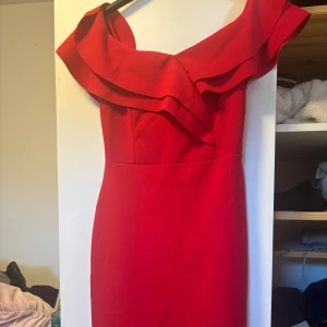 Röd offshoulder volangklänning - Snygg röd klänning med offshoulder och volangdetaljer upptill. Figurnära passform med volang längst ner på kjolen. Perfekt för dig som vill sticka ut med en klassisk men trendig look.  Skriv privat för att veta hur klänningen sitter på 