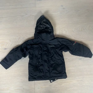 Svart vinterjacka från Nico med huva - Svart vinterjacka från Nico med huva och dragkedja framtill. Jackan har två fickor med dragkedja, diskret logga på bröstet och är tillverkad i ett slitstarkt syntetmaterial. Perfekt för kalla dagar och har en klassisk, enkel look.              ‼️Aldrig använd‼️