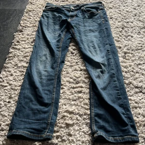 Smog 511 blå jeans, storlek 29/30 - Säljer ett par Levi's 511 jeans i klassisk blå tvätt med snygga slitningar och kontrastsömmar. Modellen har normal passform med smalare ben och fem fickor. Perfekt för dig som gillar en modern och stilren look.