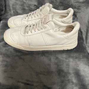 Valentino Flycrew - Säljer ett par vita Valentino Garavani sneakers i skinn med klassisk snörning och coola nitar på sulans bakkant. Skorna har en stilren design med diskreta sömmar och rund tå. Perfekta för dig som vill ha en lyxig och clean look till vardags.